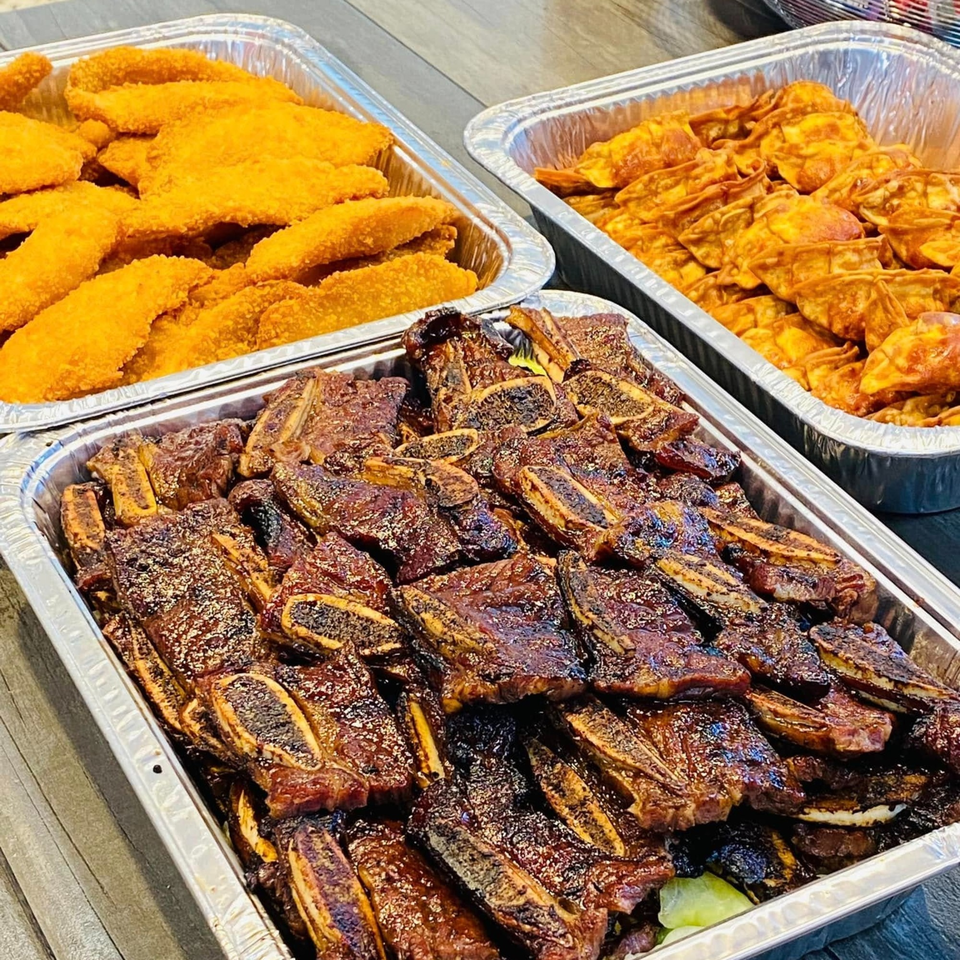 Three foil trays filled with Hawaiian BBQ short ribs, crispy chicken, and fried wontons.