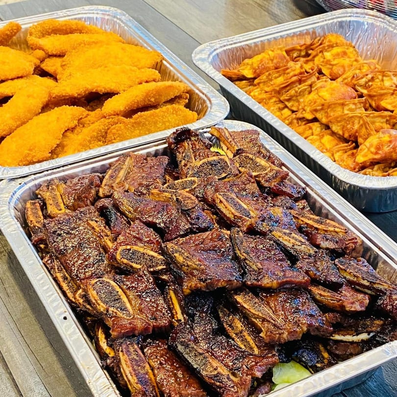Three foil trays filled with Hawaiian BBQ short ribs, crispy chicken, and fried wontons.