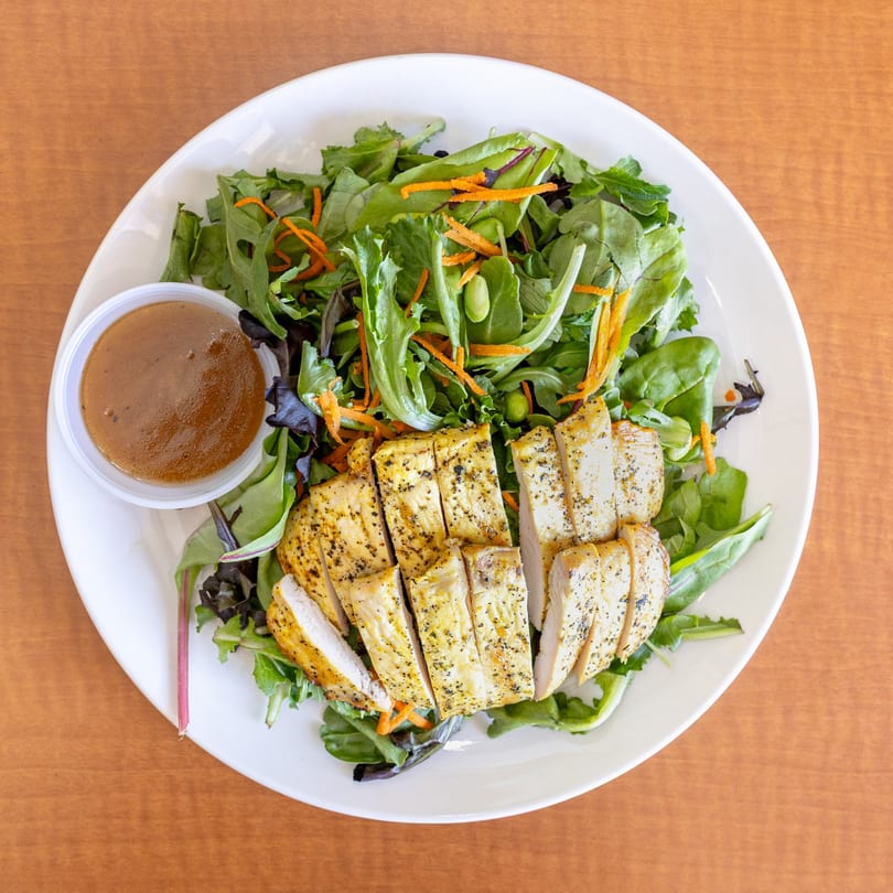 Overhead view of a Love Hawaiian BBQ chicken salad with dressing on a white plate.