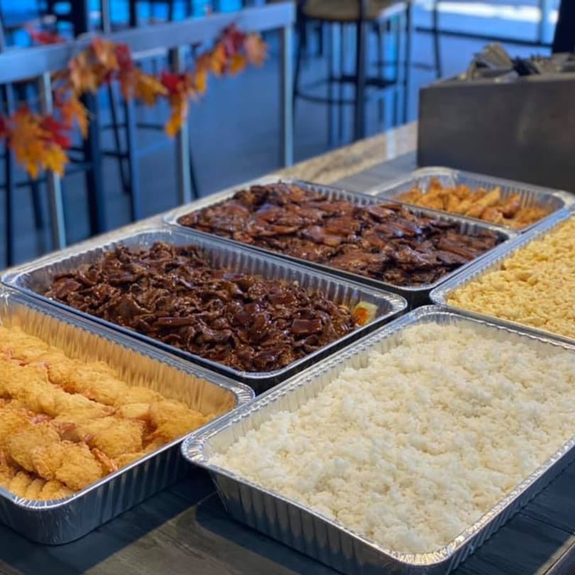 Catering trays of Hawaiian BBQ, including rice, fried shrimp, and two kinds of beef.