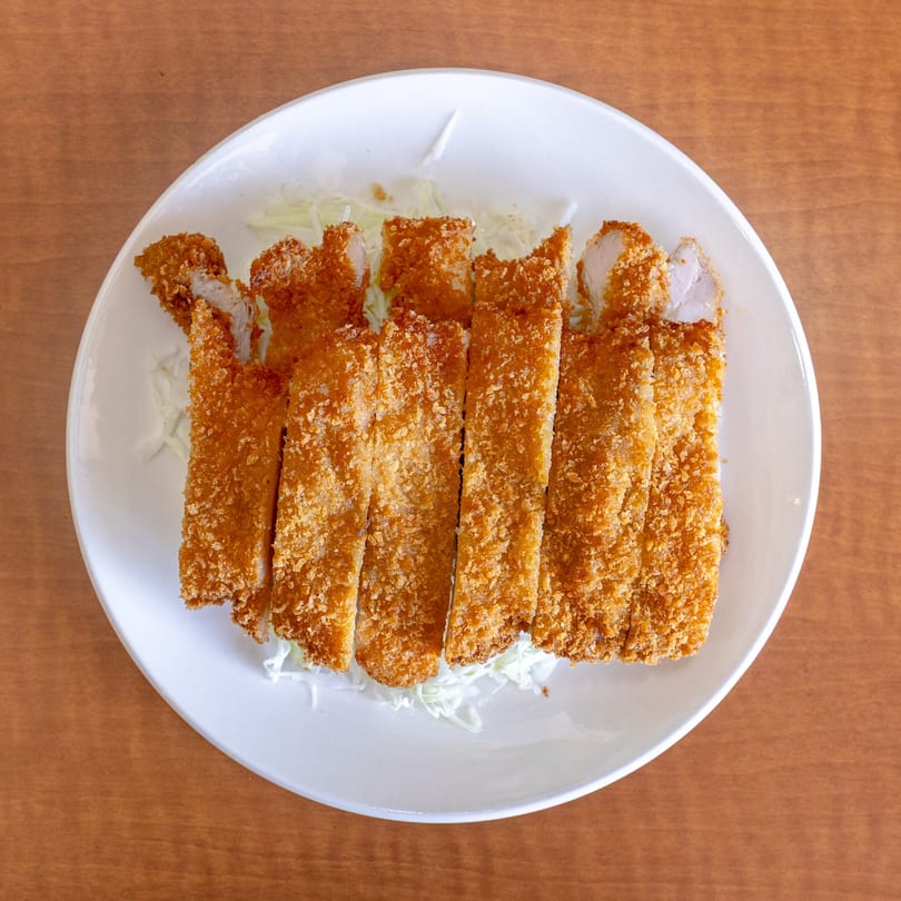 Crispy, golden-brown chicken katsu slices, served on a bed of shredded cabbage on a white plate.